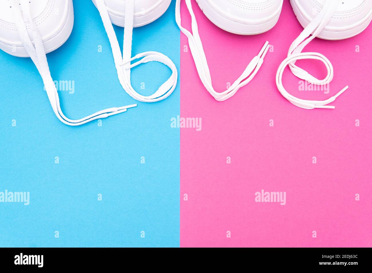 Two pairs of matching white sneakers with the lettering 'love' made of the laces on a contrast pink blue background. Matching shoes for couples idea. Stock Photo