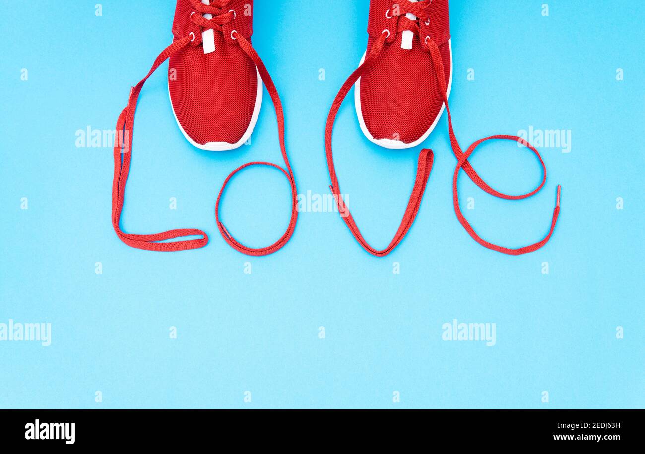 Red athletic shoes and lettering 'love' made of the shoelaces on a blue background. Fall in love with running creative concept. Stock Photo