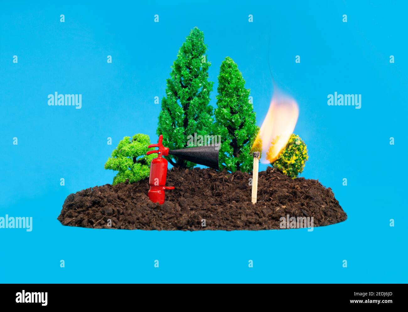 Miniature toy forest setup with a tiny fire extinguisher next to a burning match. Forest fires prevention concept. Stock Photo