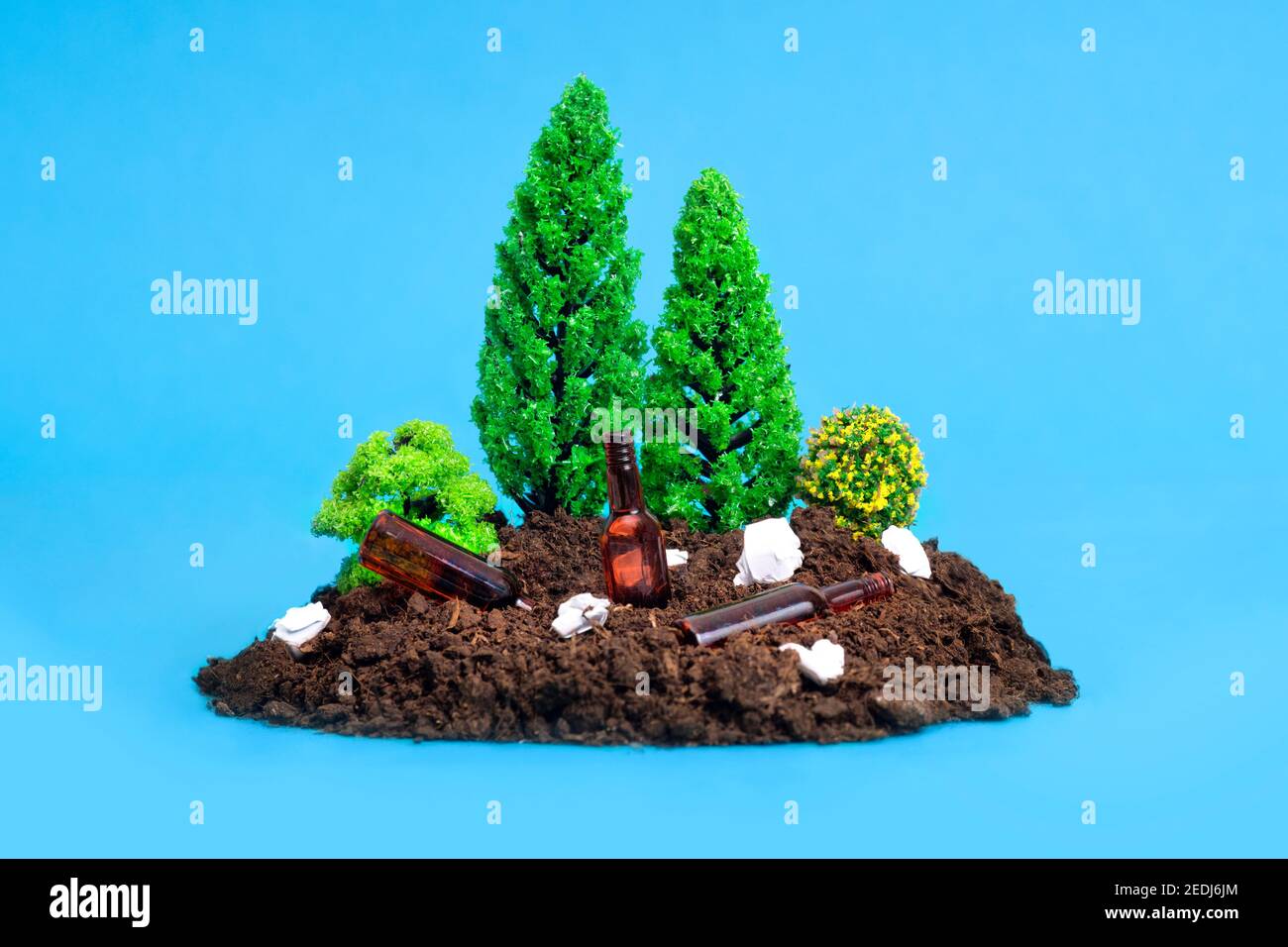 Miniature toy forest setup with paper rubbish, tiny glass bottles lying around.The concept of safe disposal of rubbish in forests and parks. Stock Photo