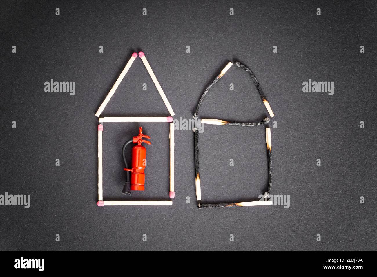 Two houses made of burnt and unburnt matches with a miniature fire extinguisher inside the undamaged one. Fire safety measures and insurance concept. Stock Photo