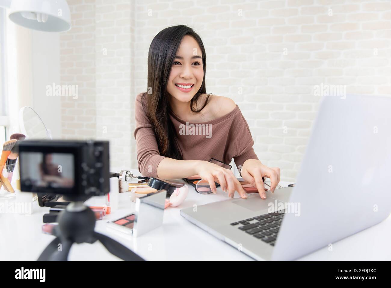 Asian woman professional beauty vlogger cheking feedback from audiences while doing cosmetic makeup tutorial live broadcasting on social media Stock Photo