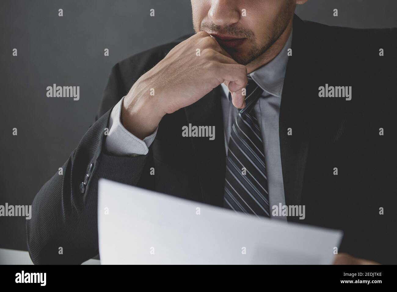 Serious businessman with hand on chin reading document and pondering Stock Photo