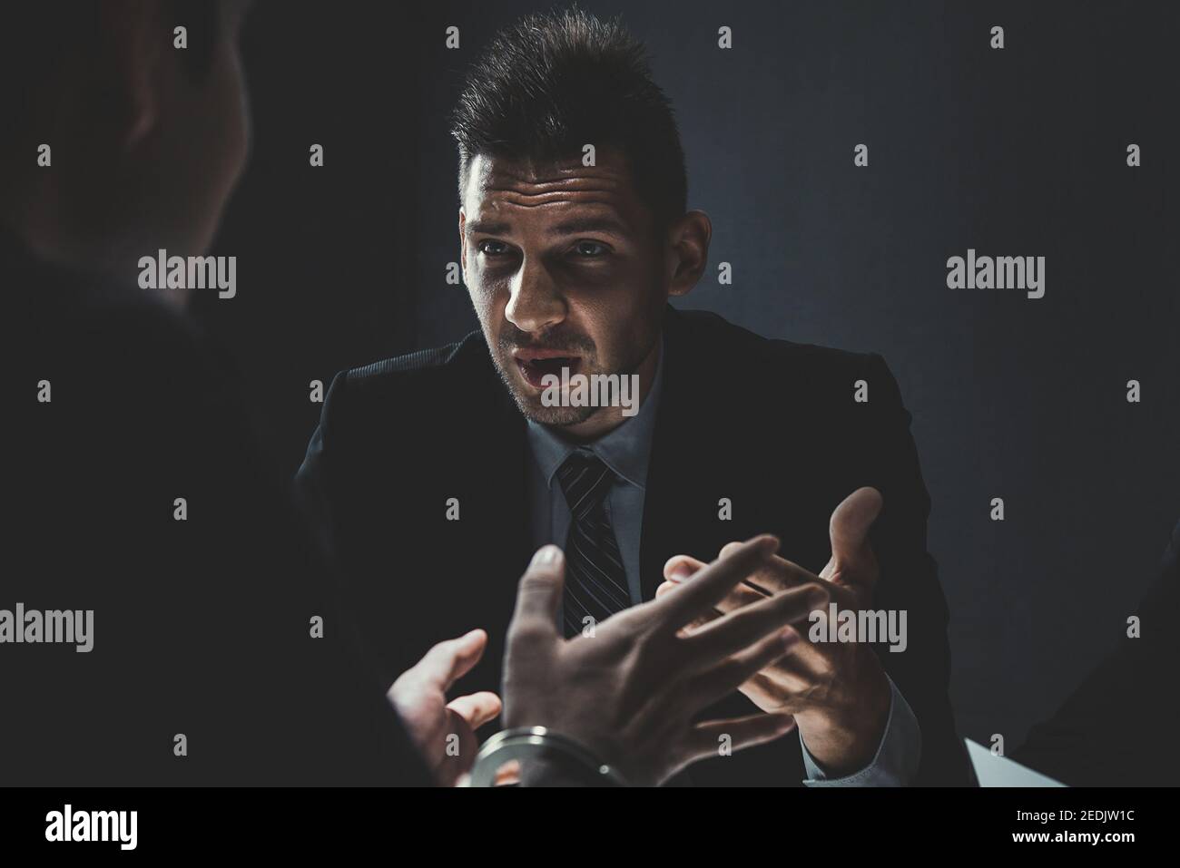 Suspect or criminal man with handcuffs being interviewed by detective in interrogation room after committed a crime Stock Photo