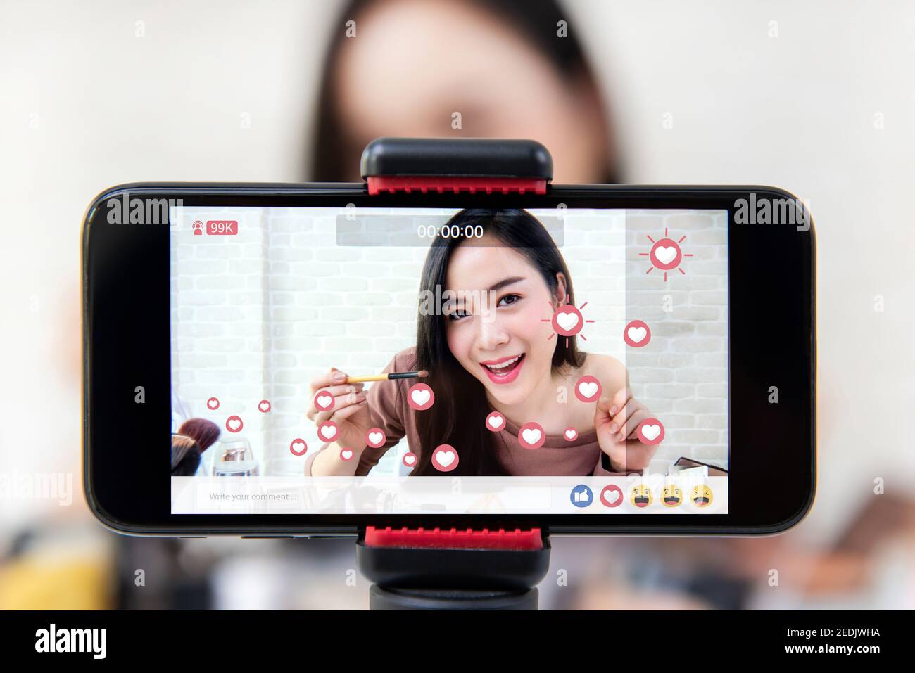 Asian woman professional beauty vlogger or blogger live broadcasting cosmetic makeup tutorial viral video clip by smartphone on social media Stock Photo