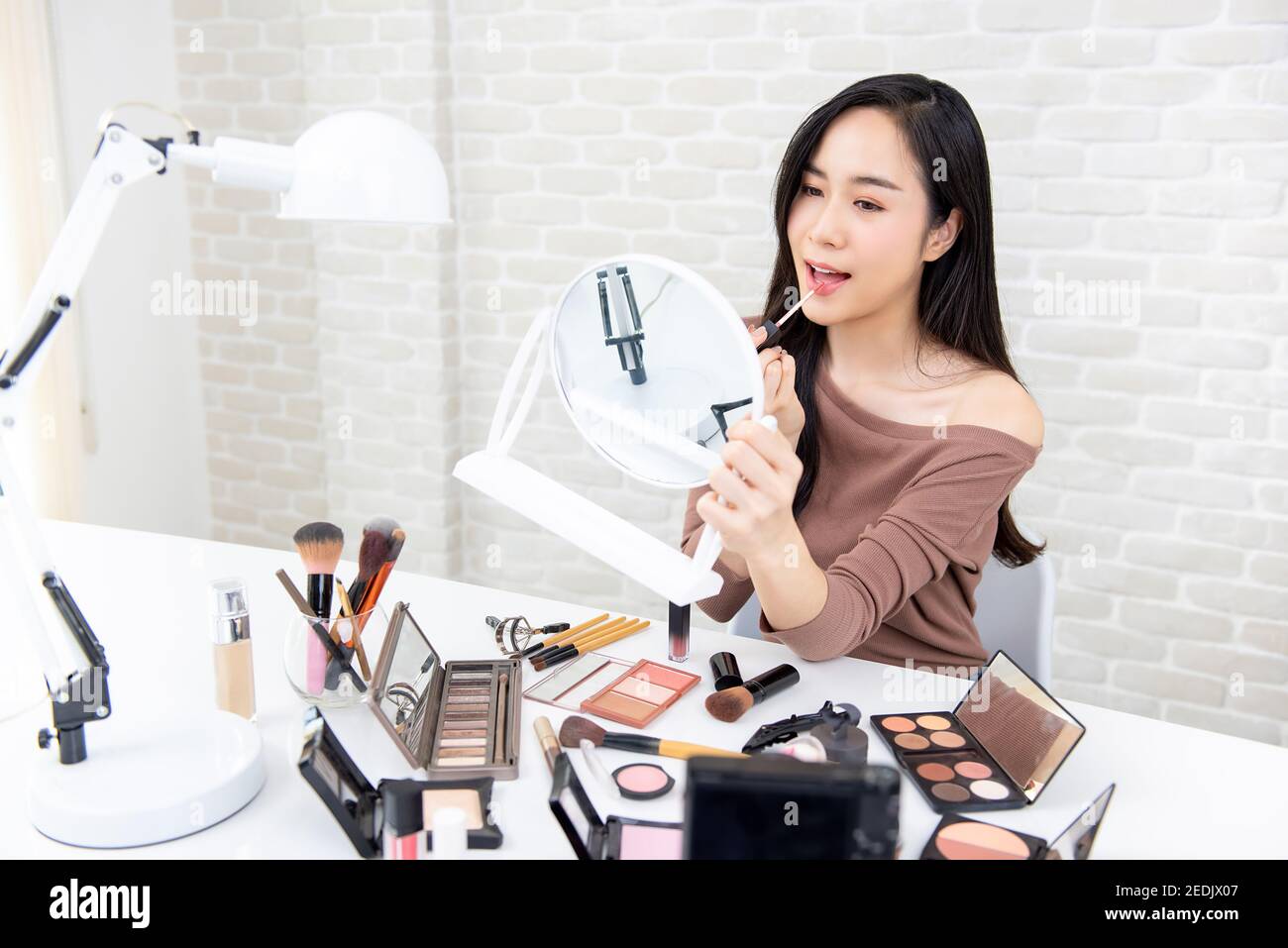 Young beautiful Asian woman professional beauty vlogger or blogger applying lipstick cream to her mouth doing cosmetic makeup tutorial Stock Photo