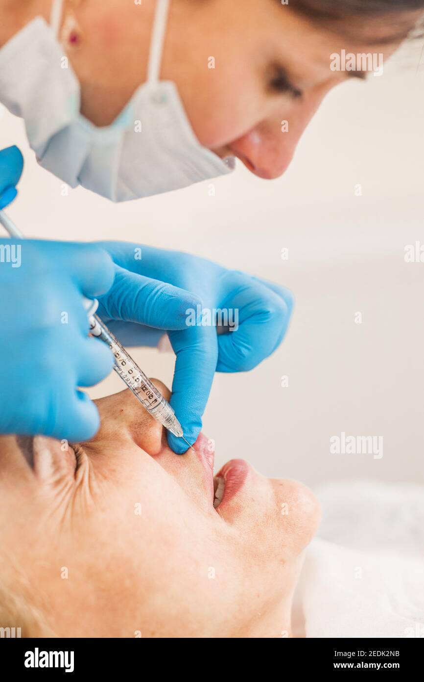 Cosmetic surgery on the skin of the face - intramuscular injection of a filler under the skin into the face of an aged woman Stock Photo