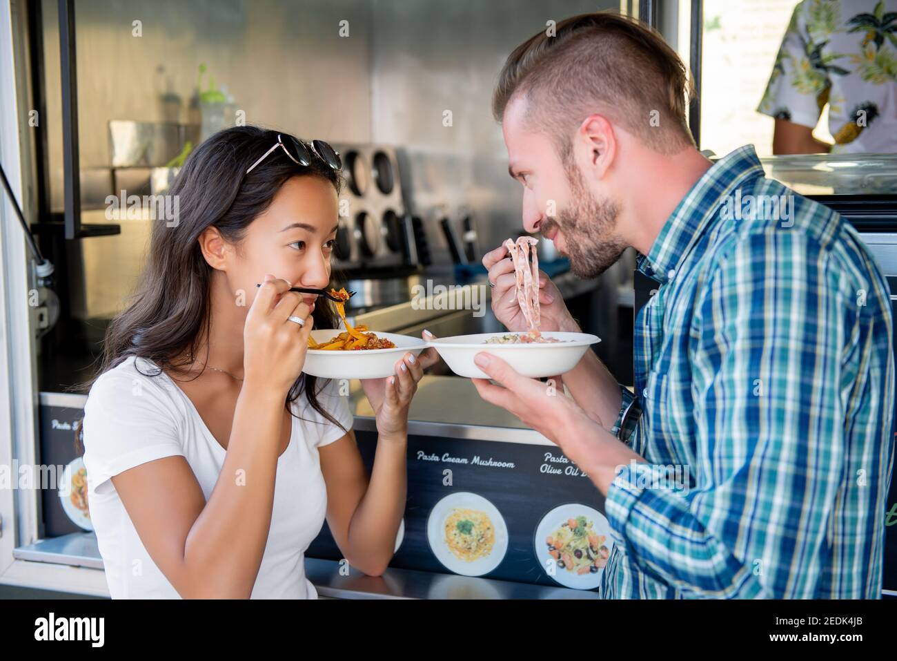 Sweet interracial couple looking in the eyes of each other while eating pasta at food truck Stock Photo