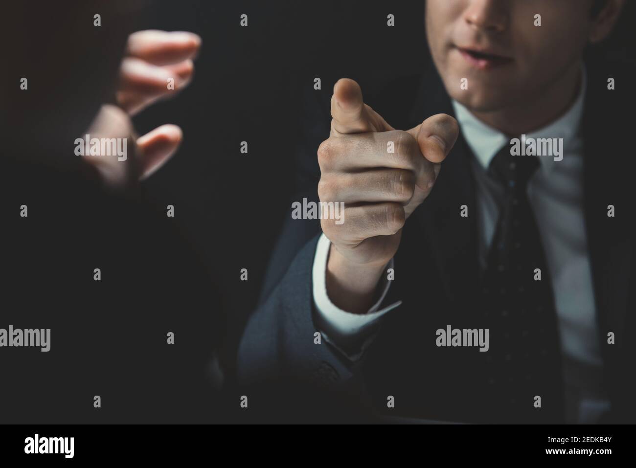 Angry man in formal business suit pointing hand to somesone he talking to in dark interrogation room Stock Photo