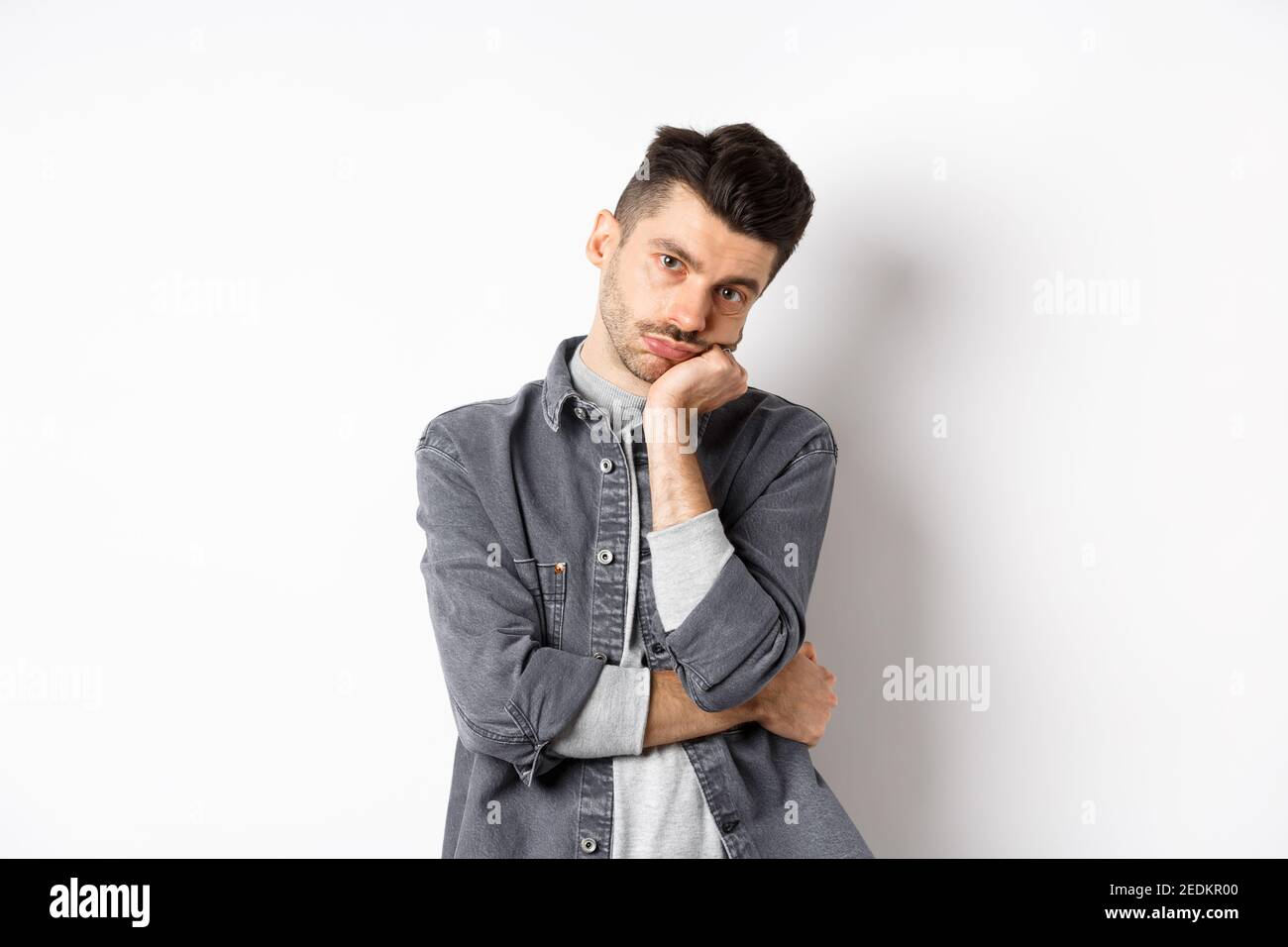 Bored and reluctant stylish guy look at camera without emotions, attend boring meeting, standing on white background Stock Photo