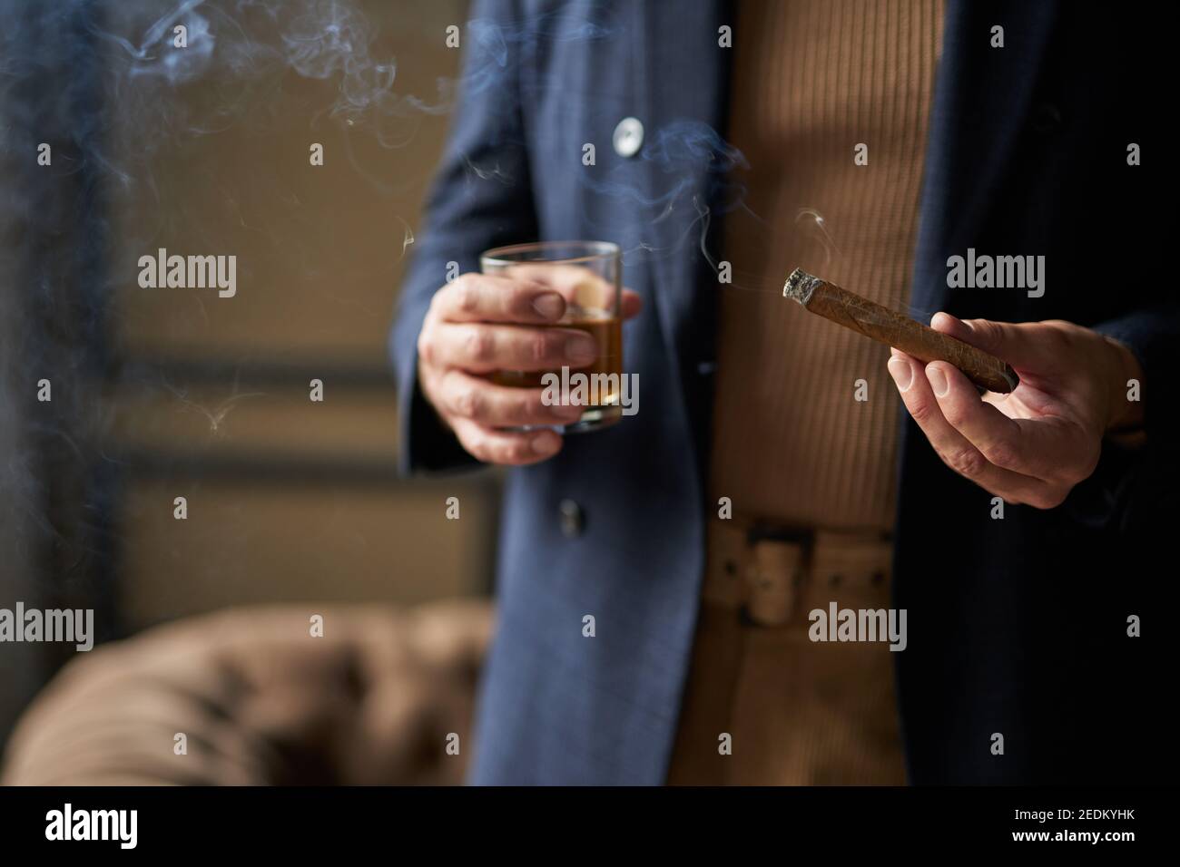 Close up shot of hand of mature man holding cigar and glass of whisky, standing indoors. Lifestyle, success, people concept Stock Photo