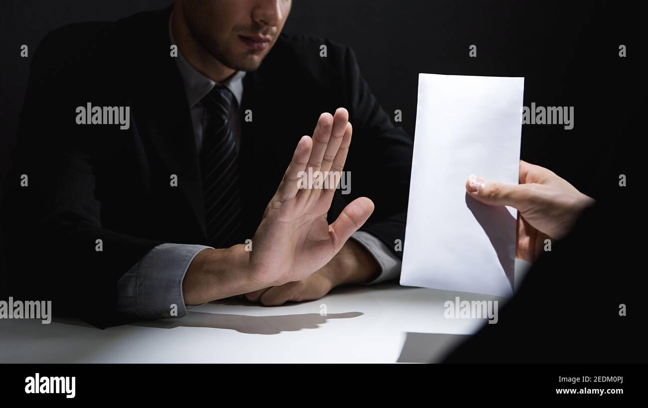 Businessman rejecting money in white envelope offered by his partner in shadow, anti bribery and corruption concept Stock Photo