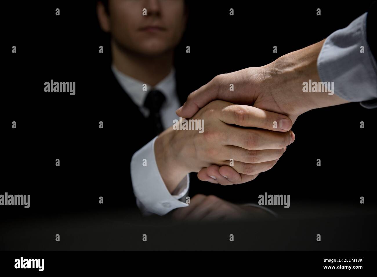 Anonymous business partners making handshake in dark shadow Stock Photo