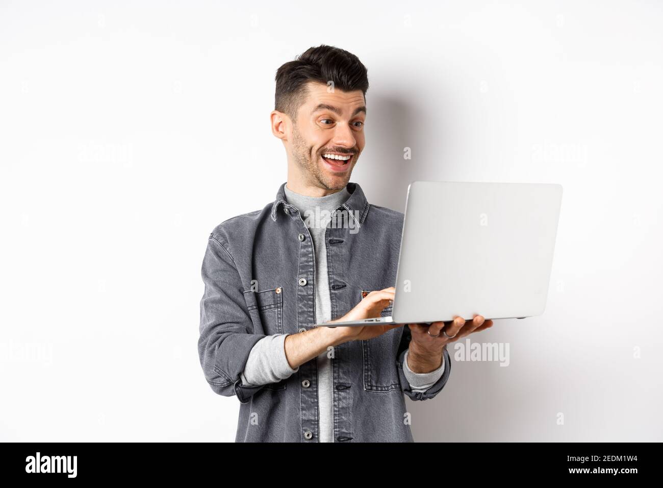 Man watching funny video on laptop, laughing at computer screen and smiling  joyful, standing on white background Stock Photo - Alamy