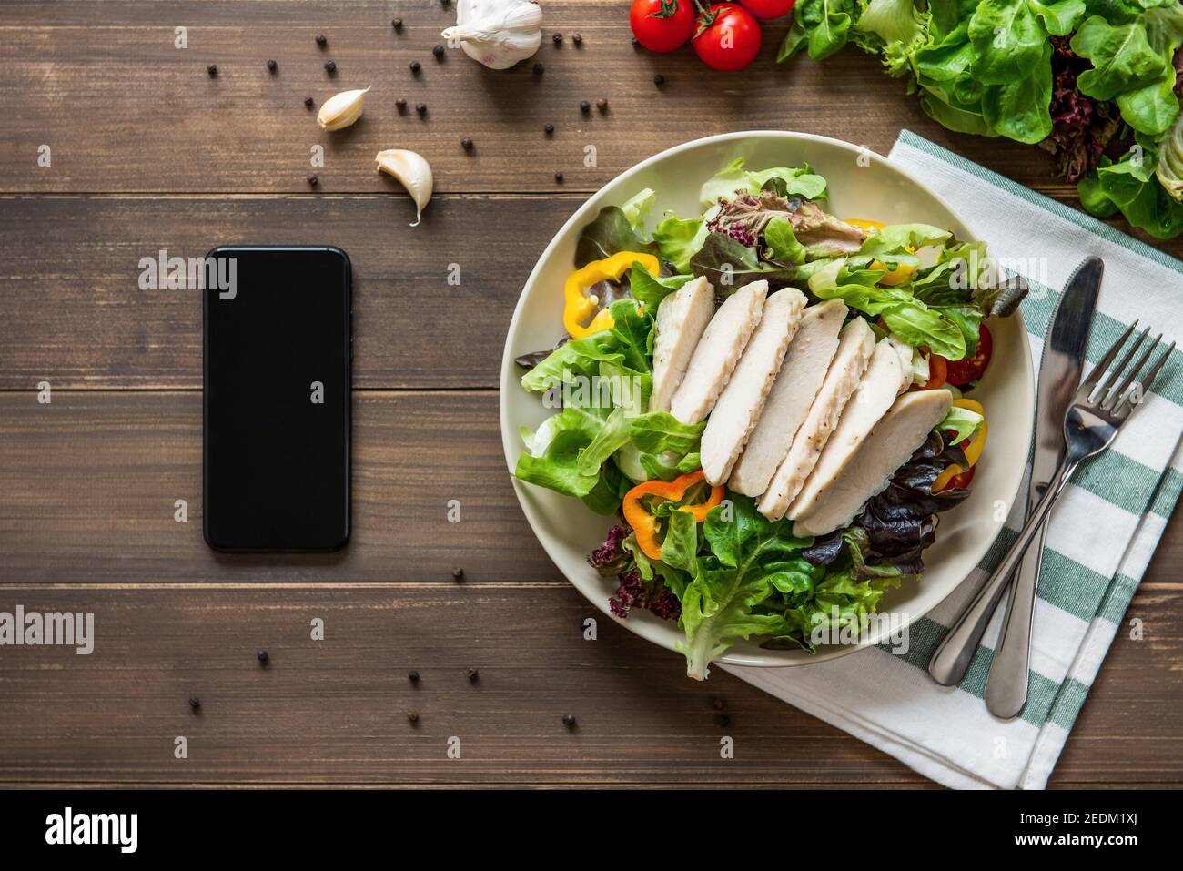 Healthy chicken salad next to smartphone on wood table background - mobile food ordering concept Stock Photo