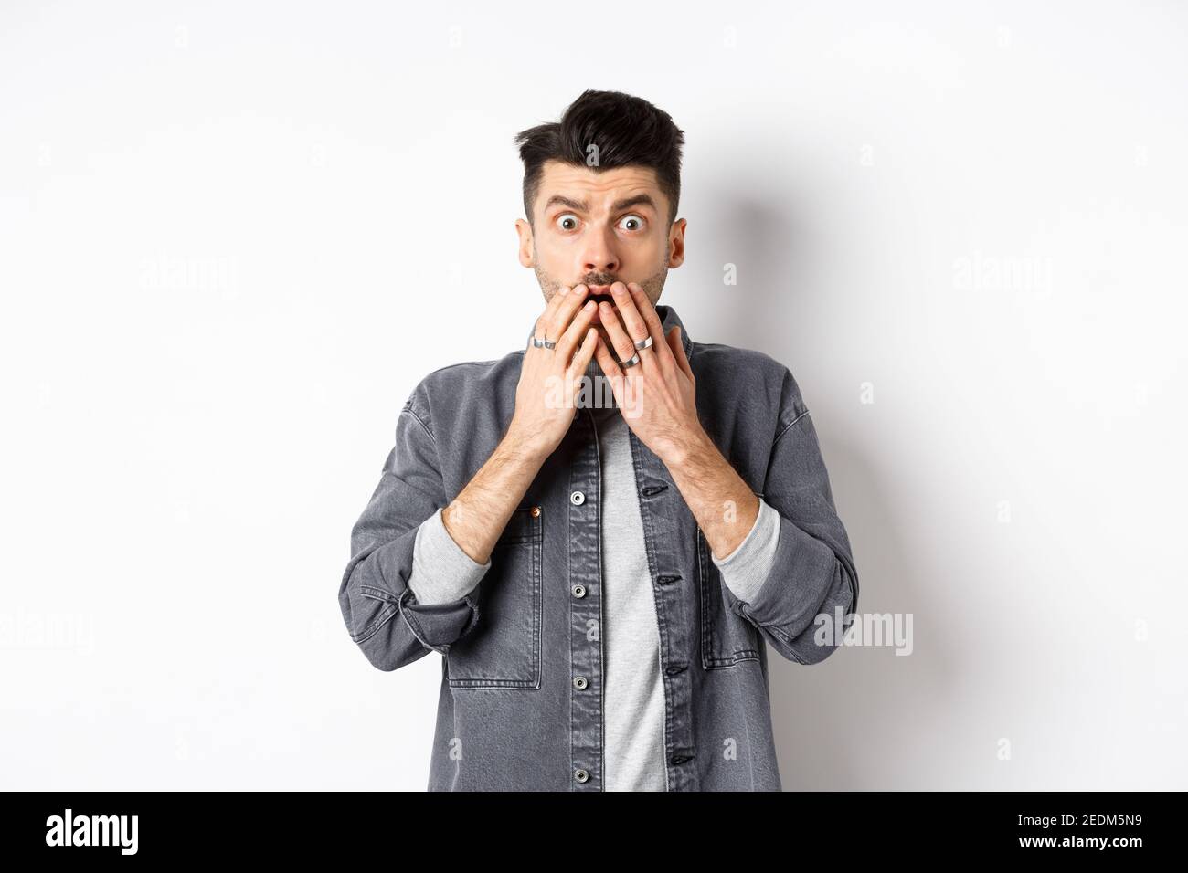 Shocked caucasian guy gasping alarmed, cover mouth with hands and ...