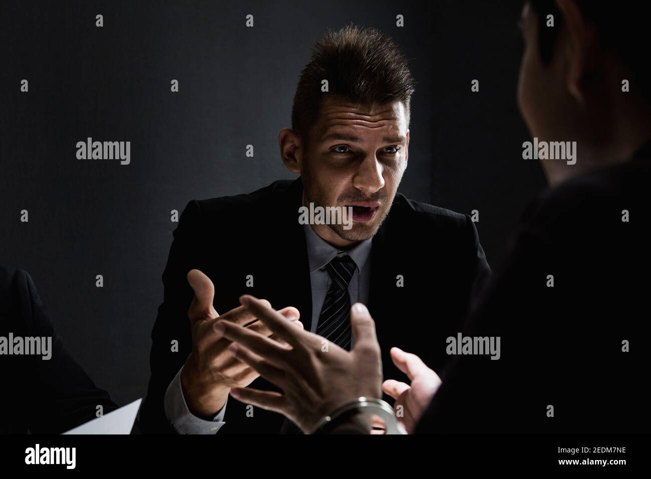 Suspect or criminal man with handcuffs being interviewed by detectives in interrogation room after committed a crime Stock Photo