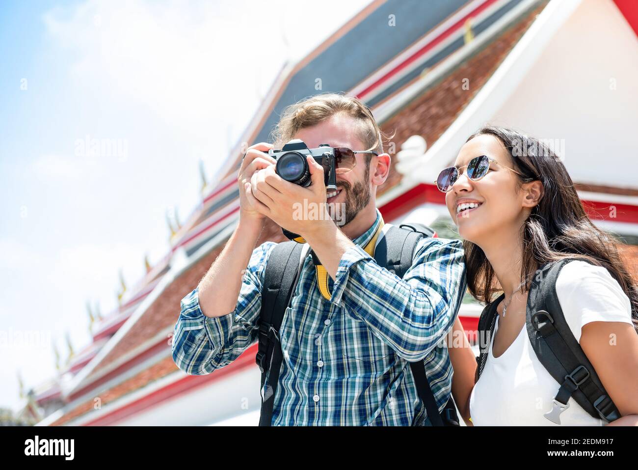 Interracial tourist couple taking photos during summer holiday trip in Bangkok Thailand with Thai temple in background Stock Photo
