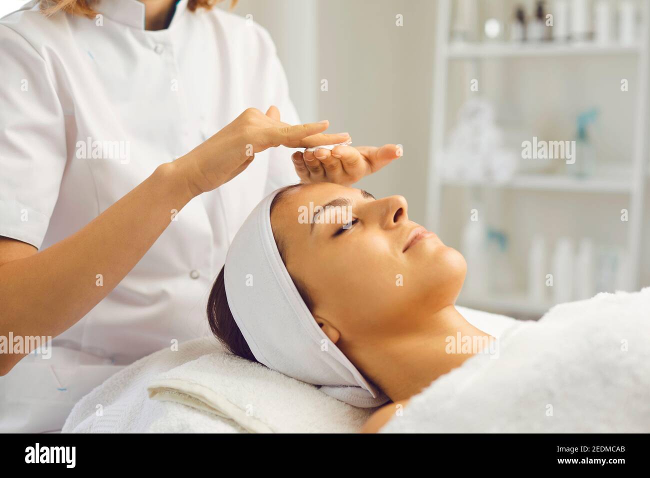 Cosmetologist rubbing cream between palms before facial massage for young woman in beauty salon Stock Photo