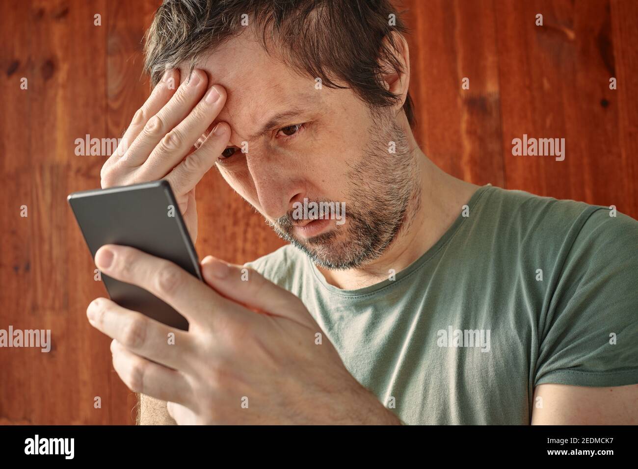 Troubled man receiving unpleasant sms message notification on mobile smart phone, reading text message in disbelief Stock Photo