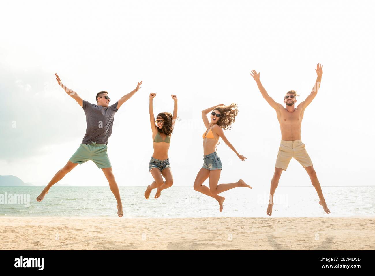 Happy young energetic group of friends jumping at the beach on summer holidays, fun and freedom concepts Stock Photo