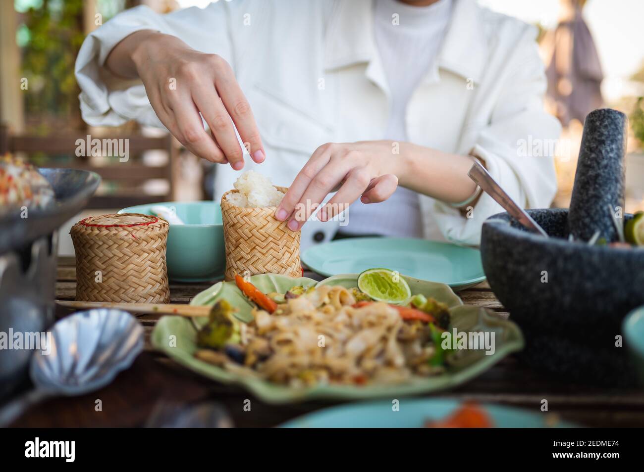 Woman opening sticky rice bamboo container while having a three course meal in a Thai restaurant closeup Stock Photo