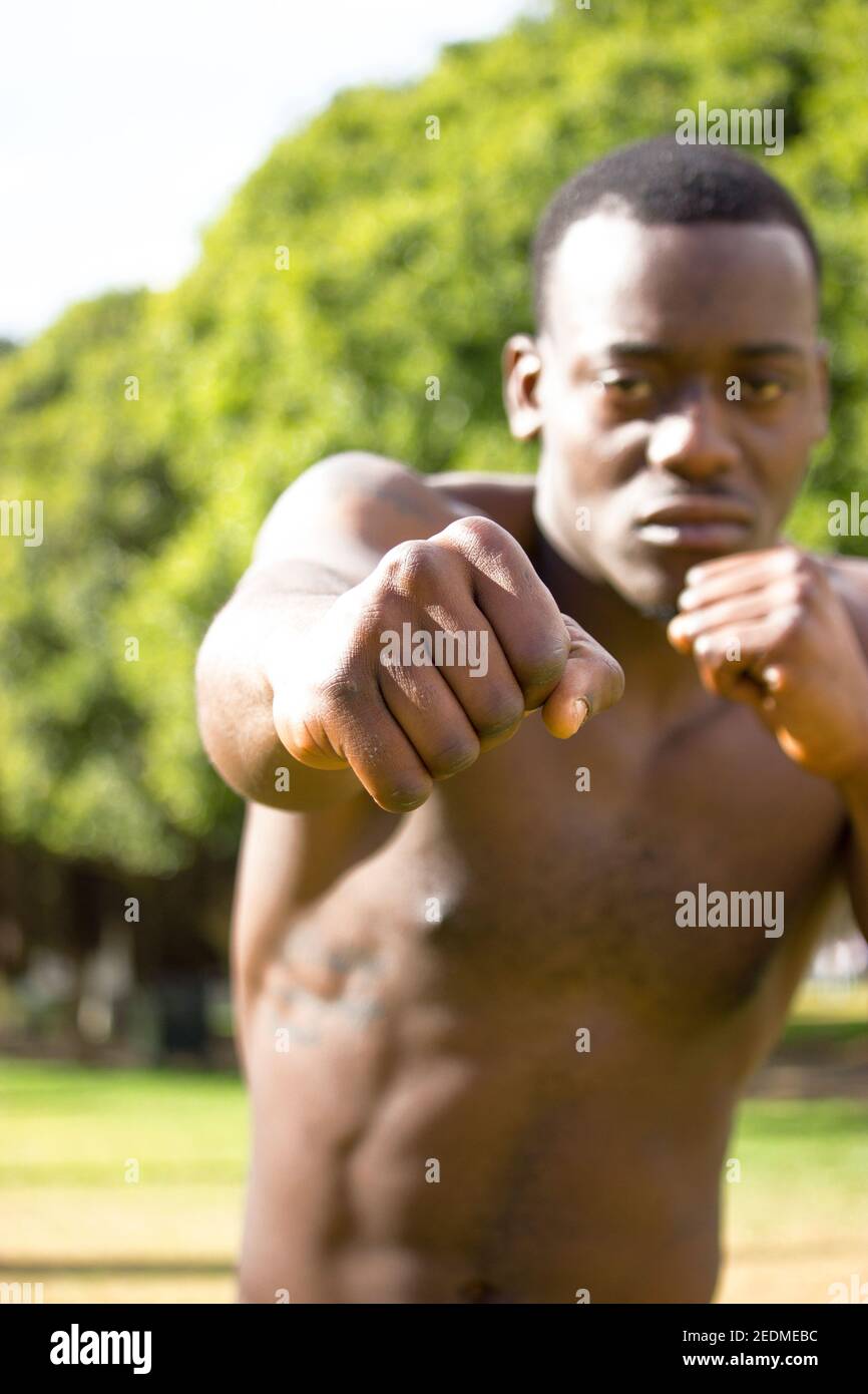 Front view of muscular black boxer punching towards camera with  a deep and intense face outdoor. Boxing and Training Concept 2021. Stock Photo