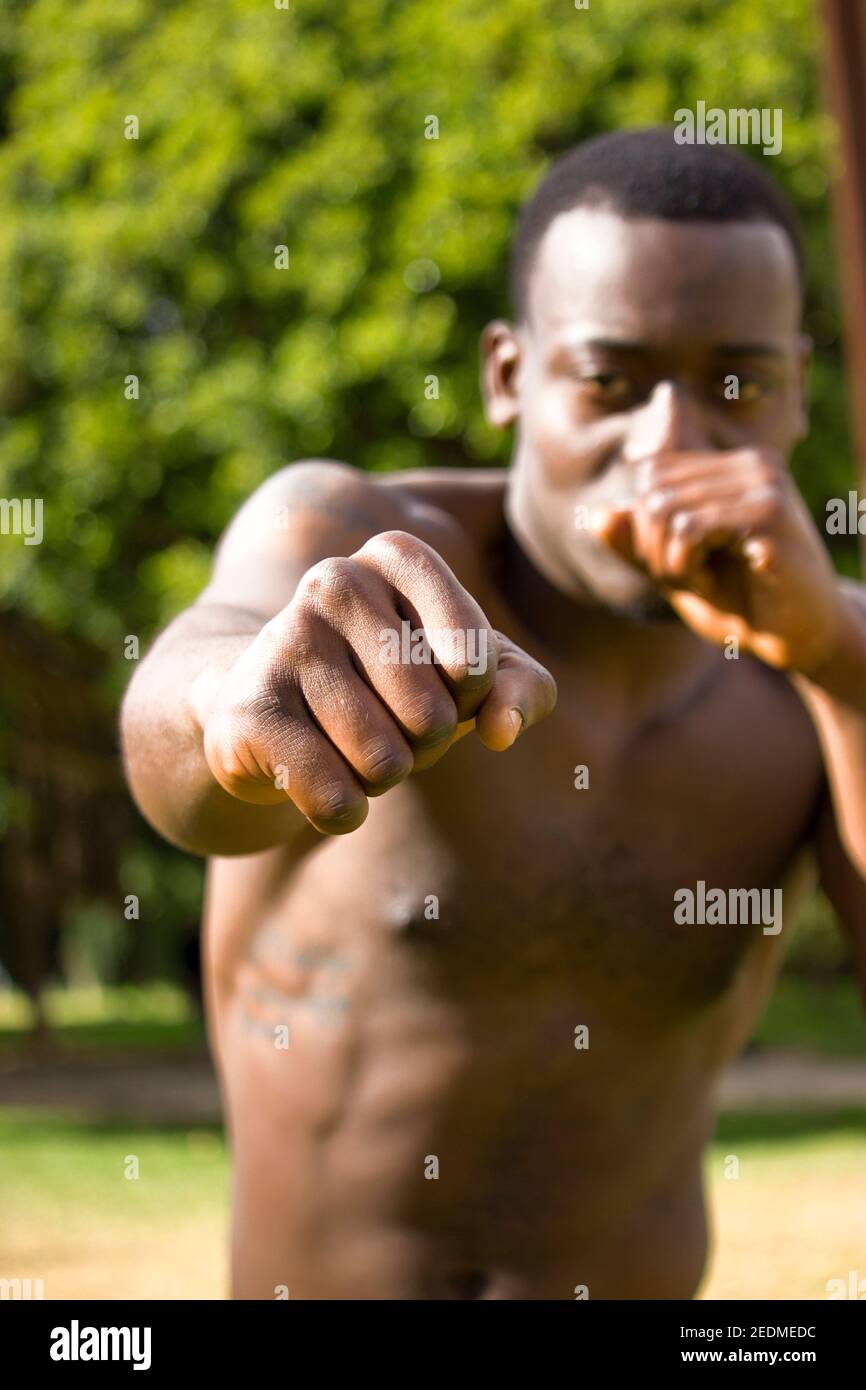 Front view of muscular black boxer out of focus punching towards camera with a deep and intense face outdoor. Boxing and Training Concept 2021. Stock Photo
