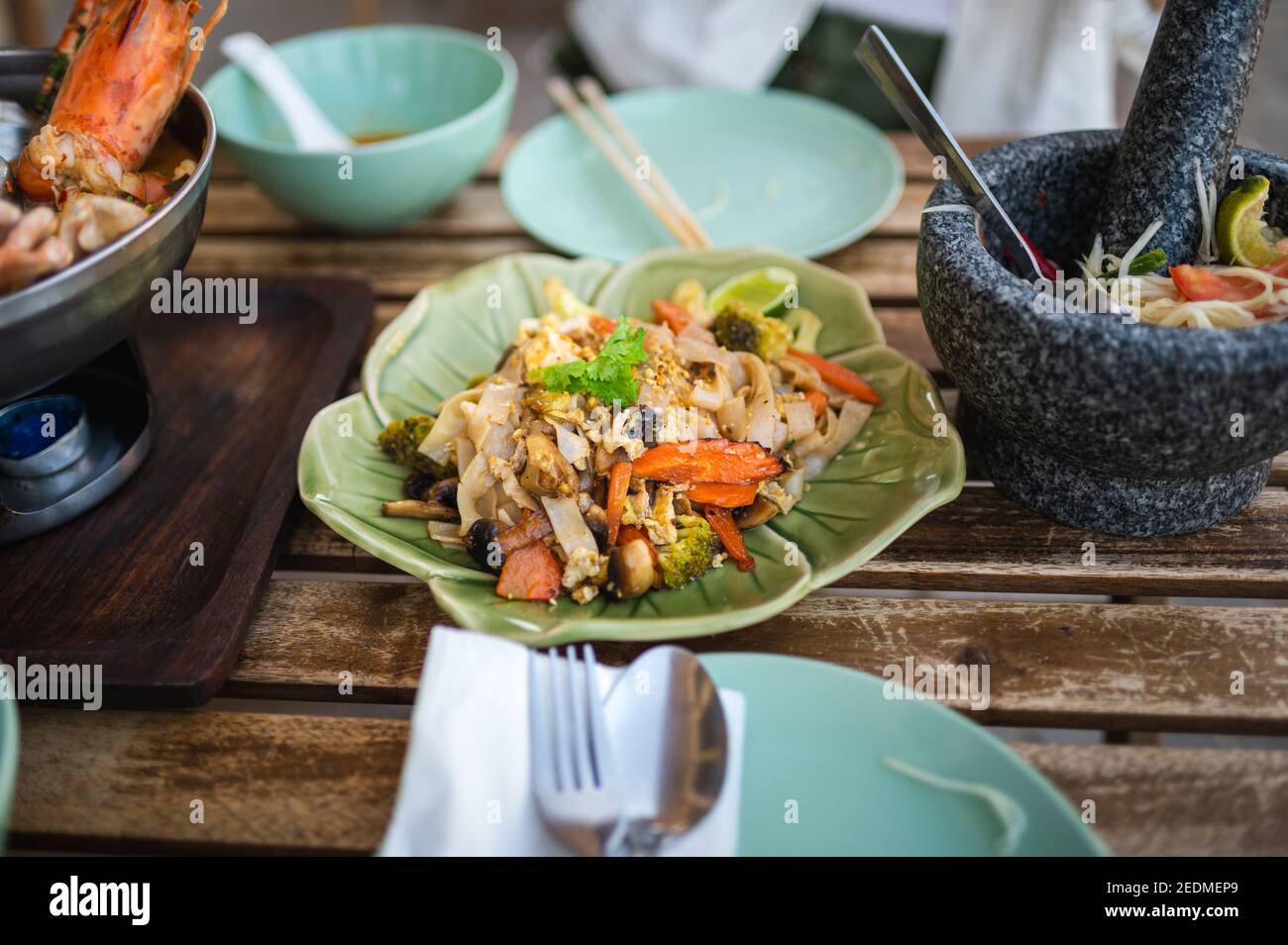 Pad see ew stir fried noodles on a table with Thai food dishes closeup Stock Photo