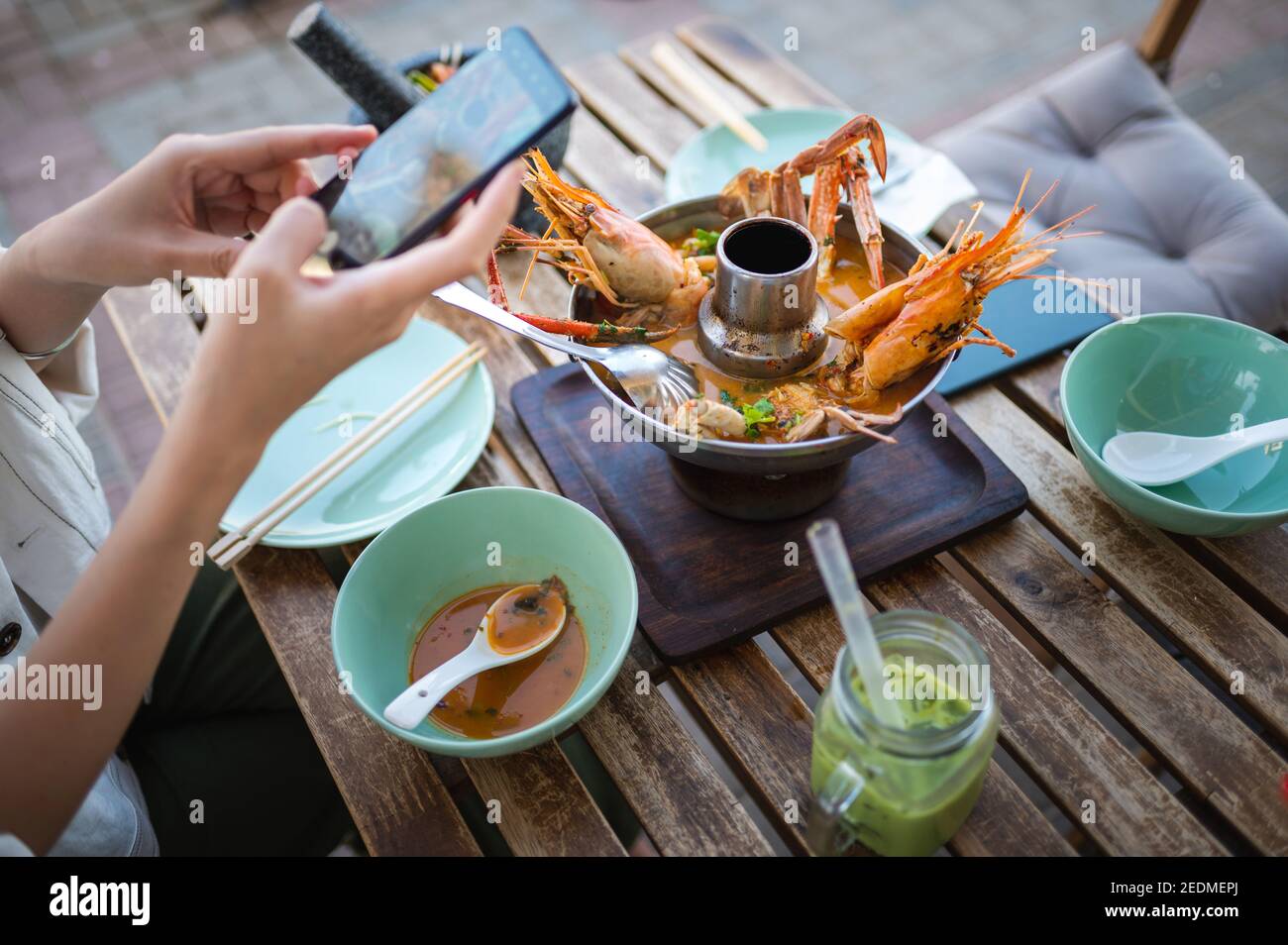 Woman taking photo of a Thai Tom Yum soup with prawns and crab while having a meal in a restaurant Stock Photo