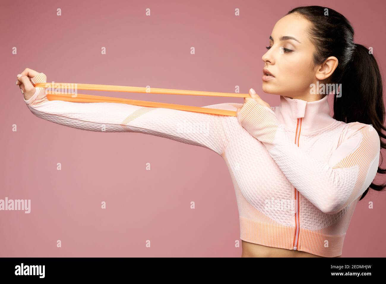 Attractive sporty lady doing exercise with elastic resistance band. Isolated on pink background Stock Photo