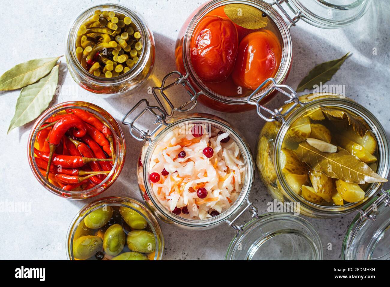Homemade pickled or fermented vegetables - sauerkraut, wild garlic, chili, pickles, pickled tomatoes and olives in glass jars. Stock Photo