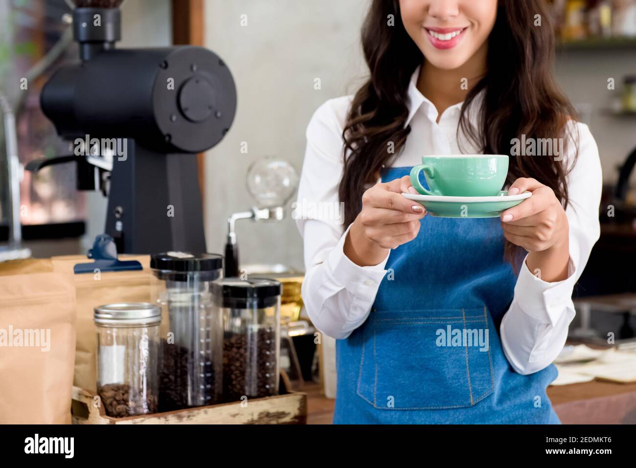 Young smiling female barista serving a cup of coffee in cafe Stock Photo
