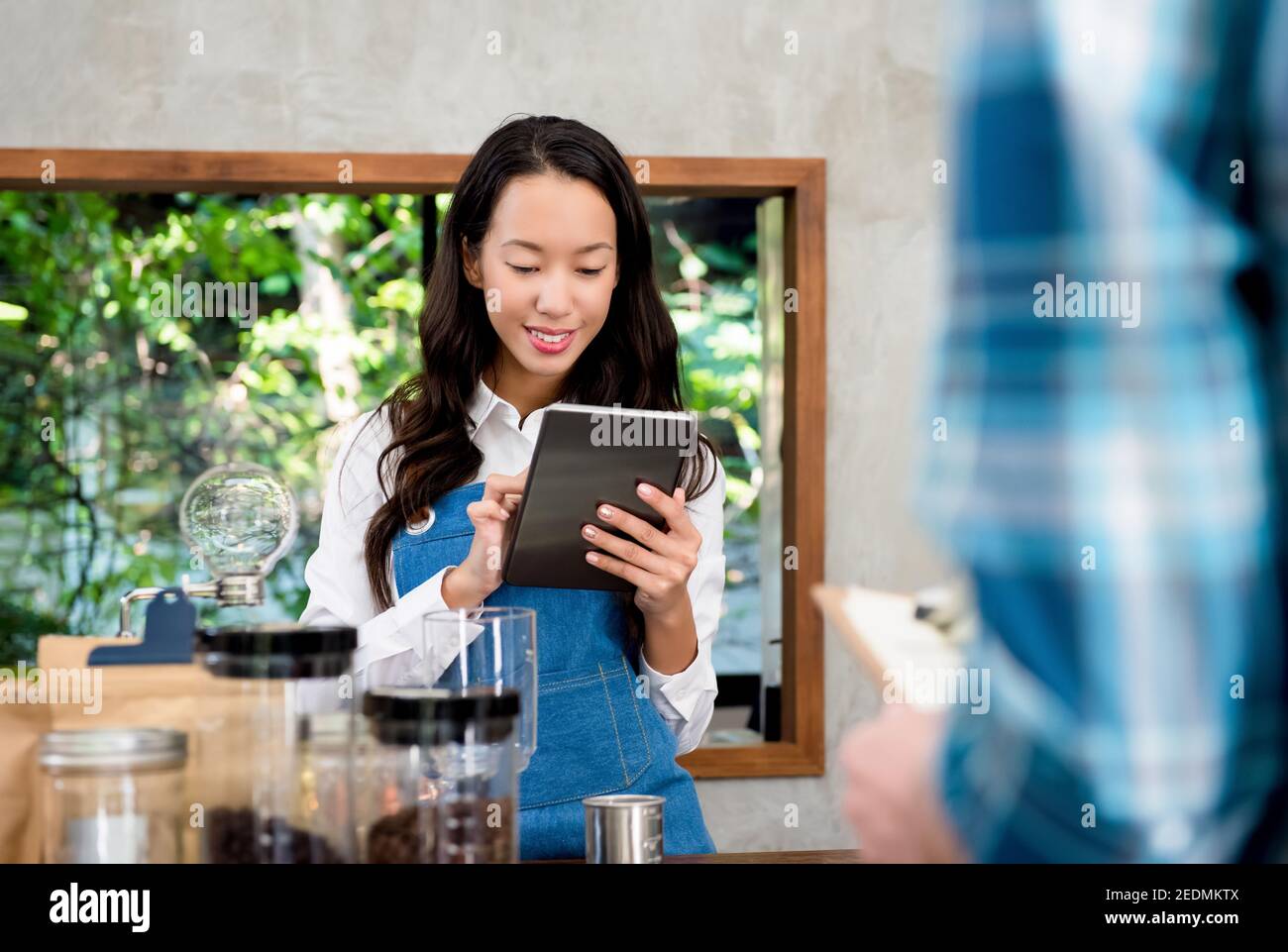 Young Asian female staff taking order from customer with tablet computer at counter in coffee shop Stock Photo