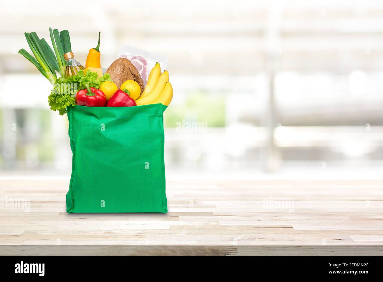 Food and groceries in green eco-friendly reusable shopping bag on wood table with blurred kitchen background Stock Photo