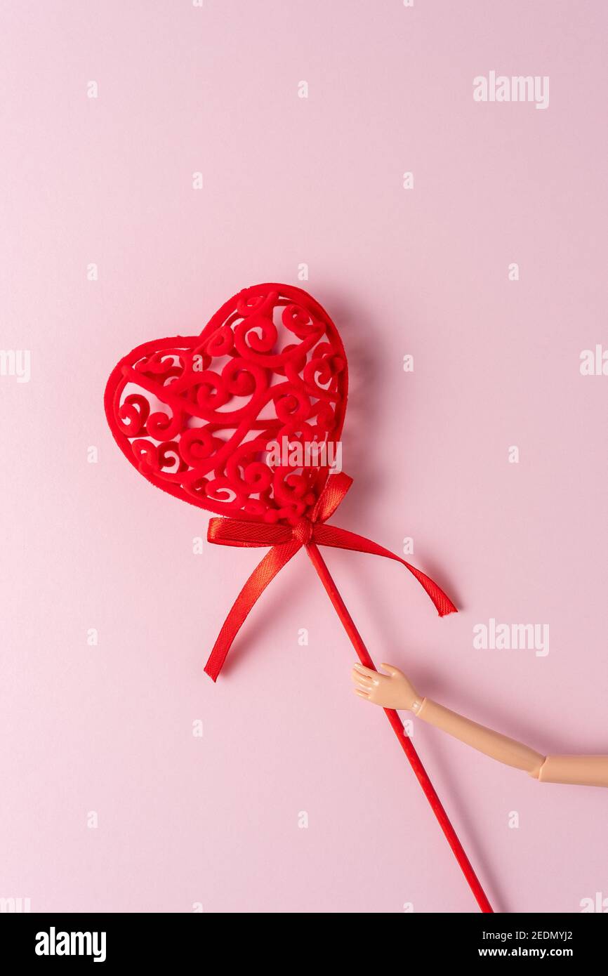 Hand of a doll with red heart on a pink background. Love minimal ...