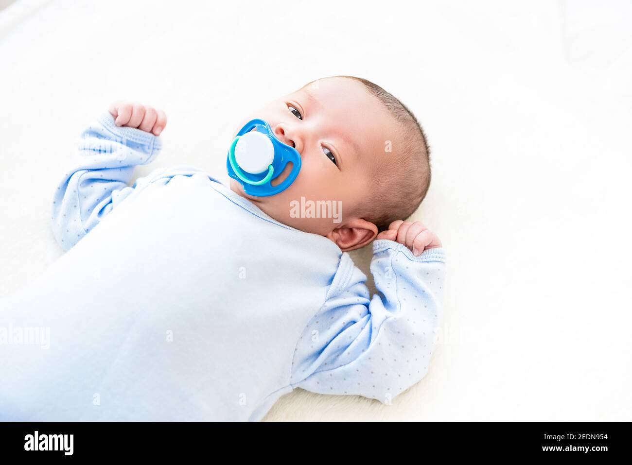 Adorable little newborn baby lying on white bed sheet with dummy in her