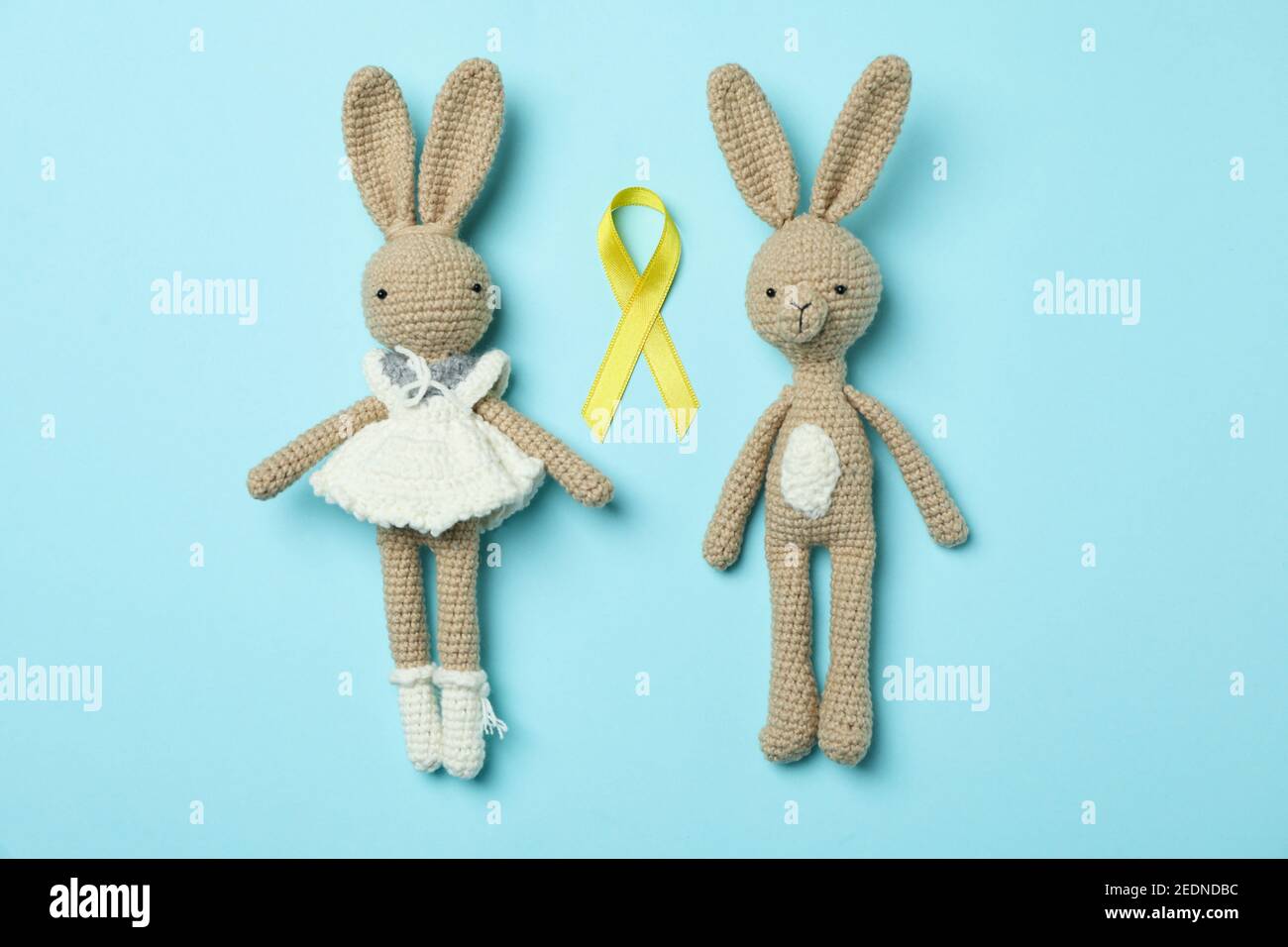 Toy bunnies and childhood cancer awareness ribbon on blue background Stock Photo