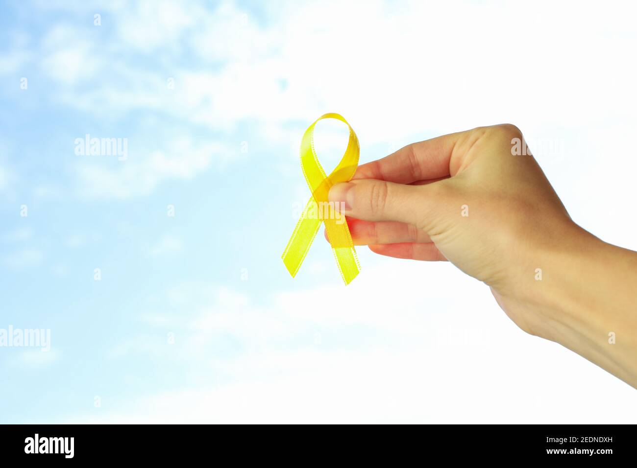 Female hand hold childhood cancer awareness ribbon on sky background Stock Photo