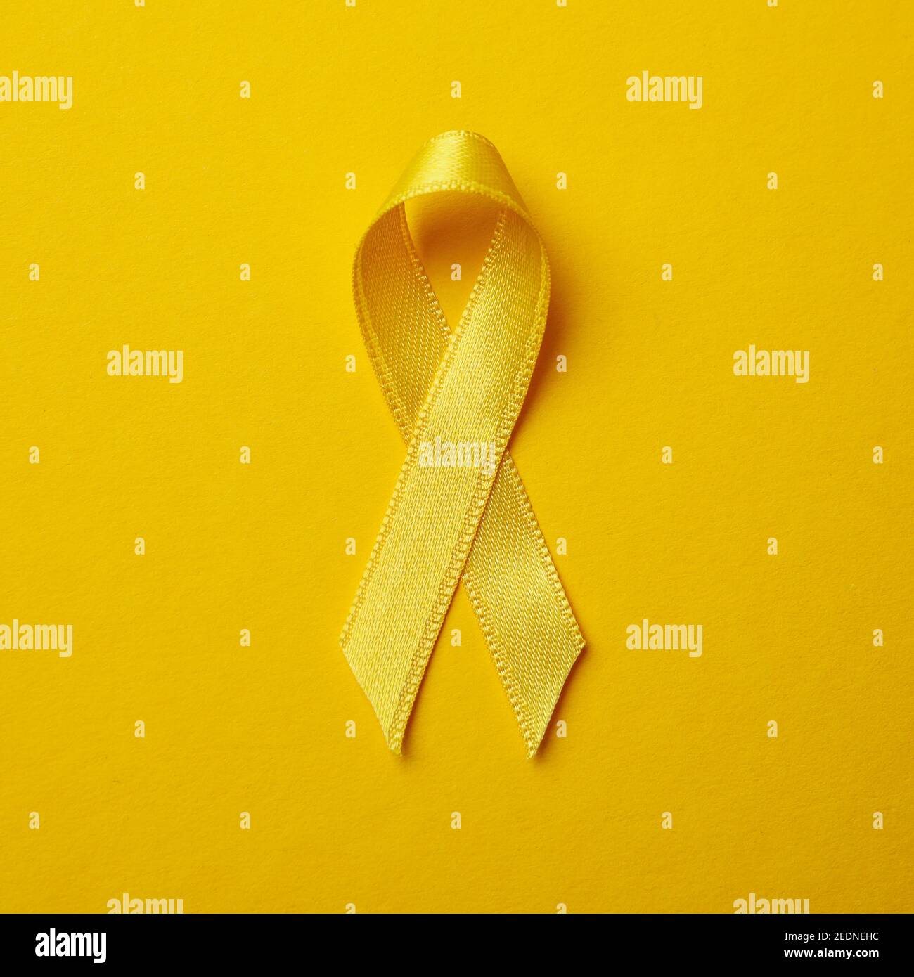 Childhood cancer awareness ribbon on yellow background Stock Photo