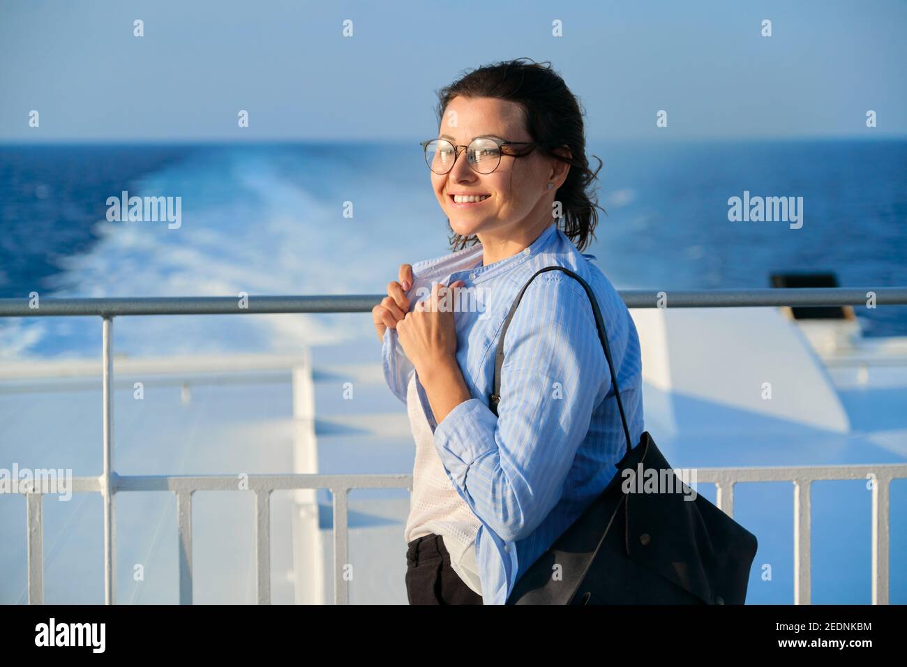 Female in blue shirt on the deck of ship looking at seascape, sky sea sunset background Stock Photo