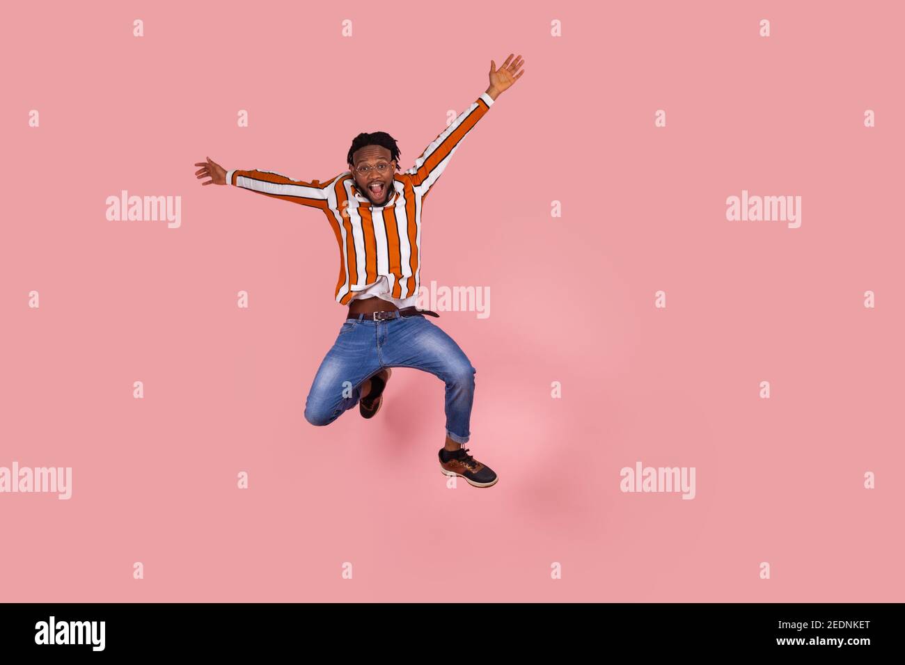 Excited afro-american man with dreadlocks highly jumping and rising hands, pretending he is flying, looking at camera with satisfied surprised express Stock Photo