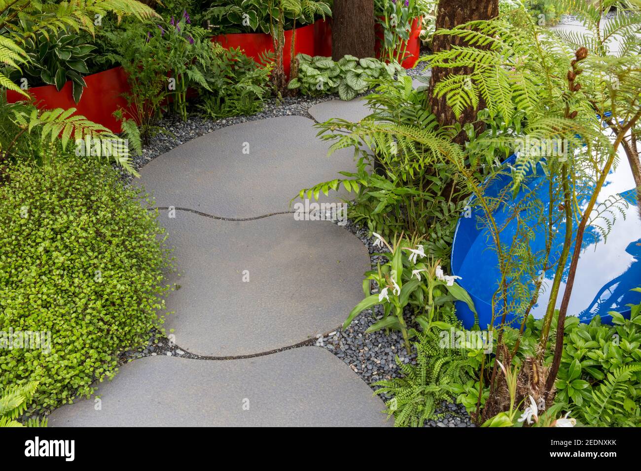 A modern stone paving paved garden path with a water feature with a green evergreen garden border ferns Hampton Court Flower Show London England UK Stock Photo
