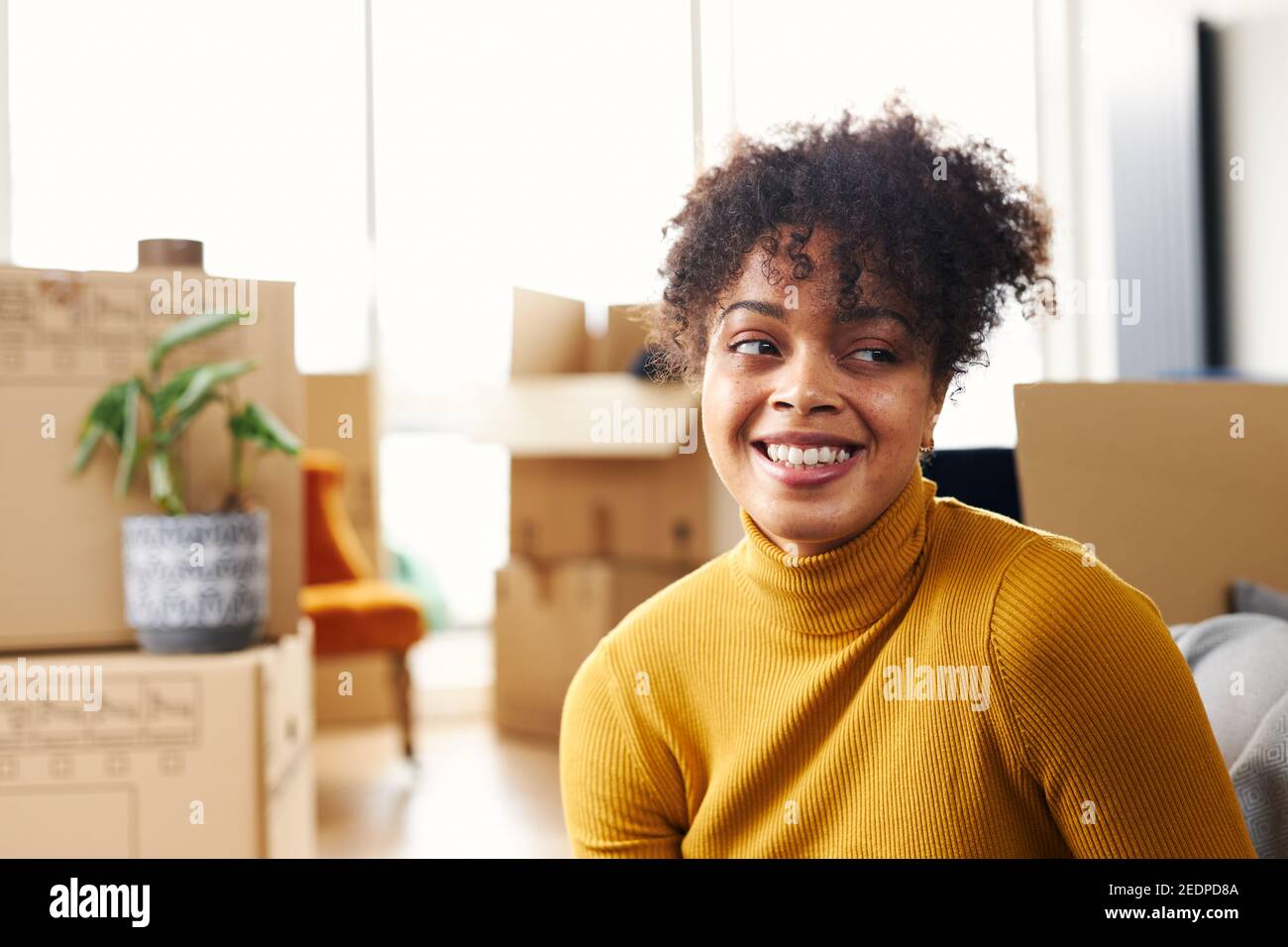 Portrait of happy young woman sitting on floor in lounge of new home ...