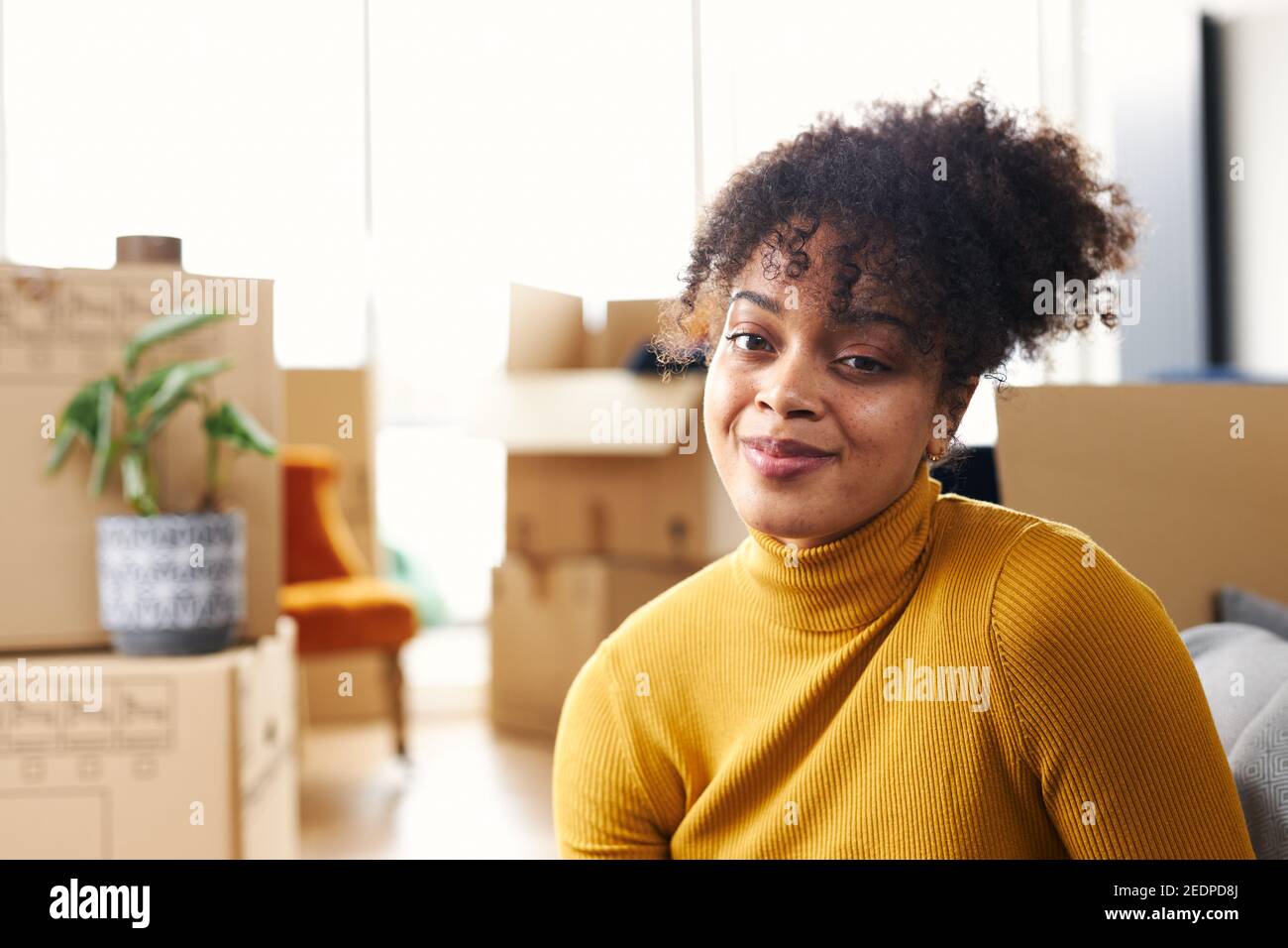 Portrait of happy young woman sitting on floor in lounge of new home ...