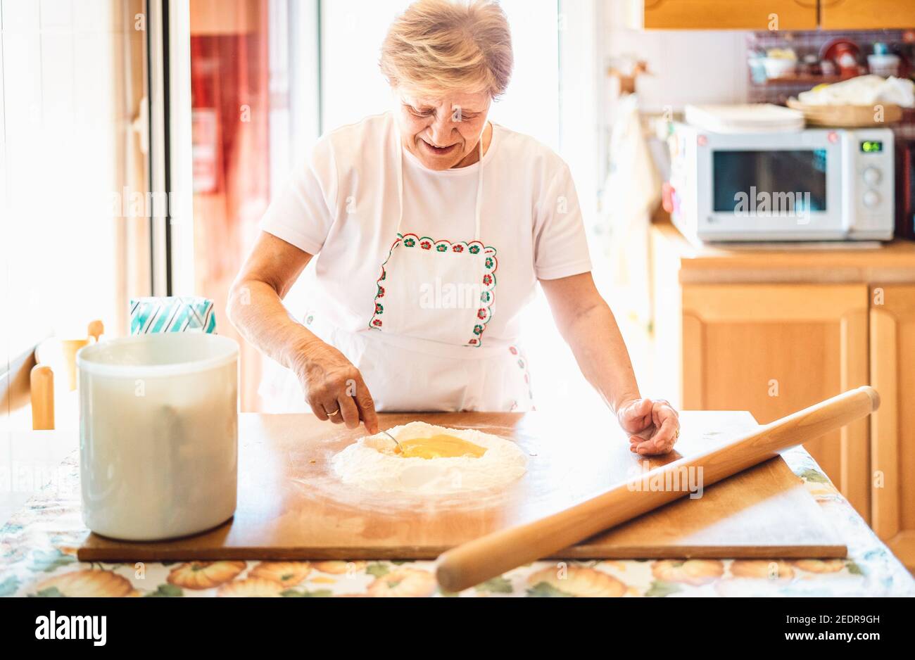 Happy woman preparing handmade receipt at house kitchen - Local food concept with home made italian pasta preparation - Warm bright backlight filter Stock Photo