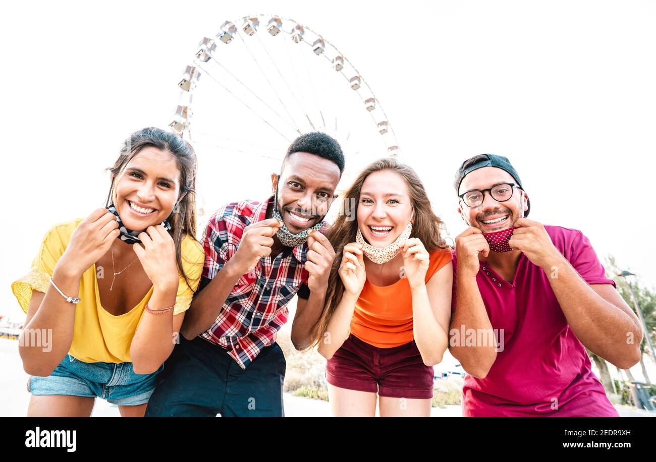 Multicultural people taking happy photo with open face masks after lockdown reopening - New normal lifestyle concept with young friends having fun Stock Photo