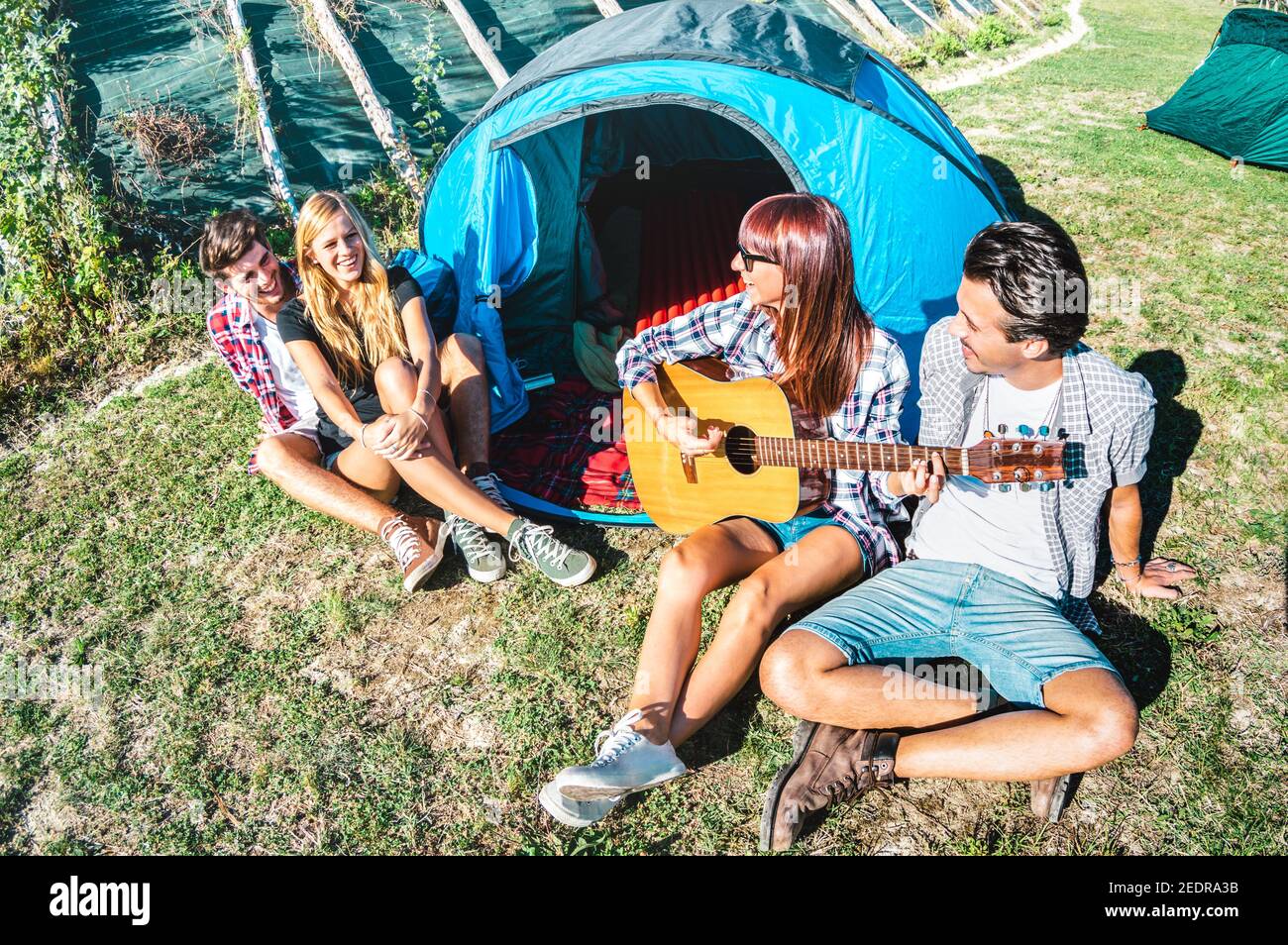 Friends group having fun outdoor singing at picnic camp with vintage guitar - Young people enjoying summer time together at countryside party Stock Photo
