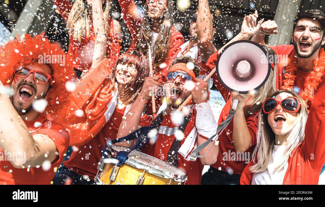 Friends football supporter fans cheering with confetti watching soccer match event at stadium - Young people group with red t-shirts Stock Photo
