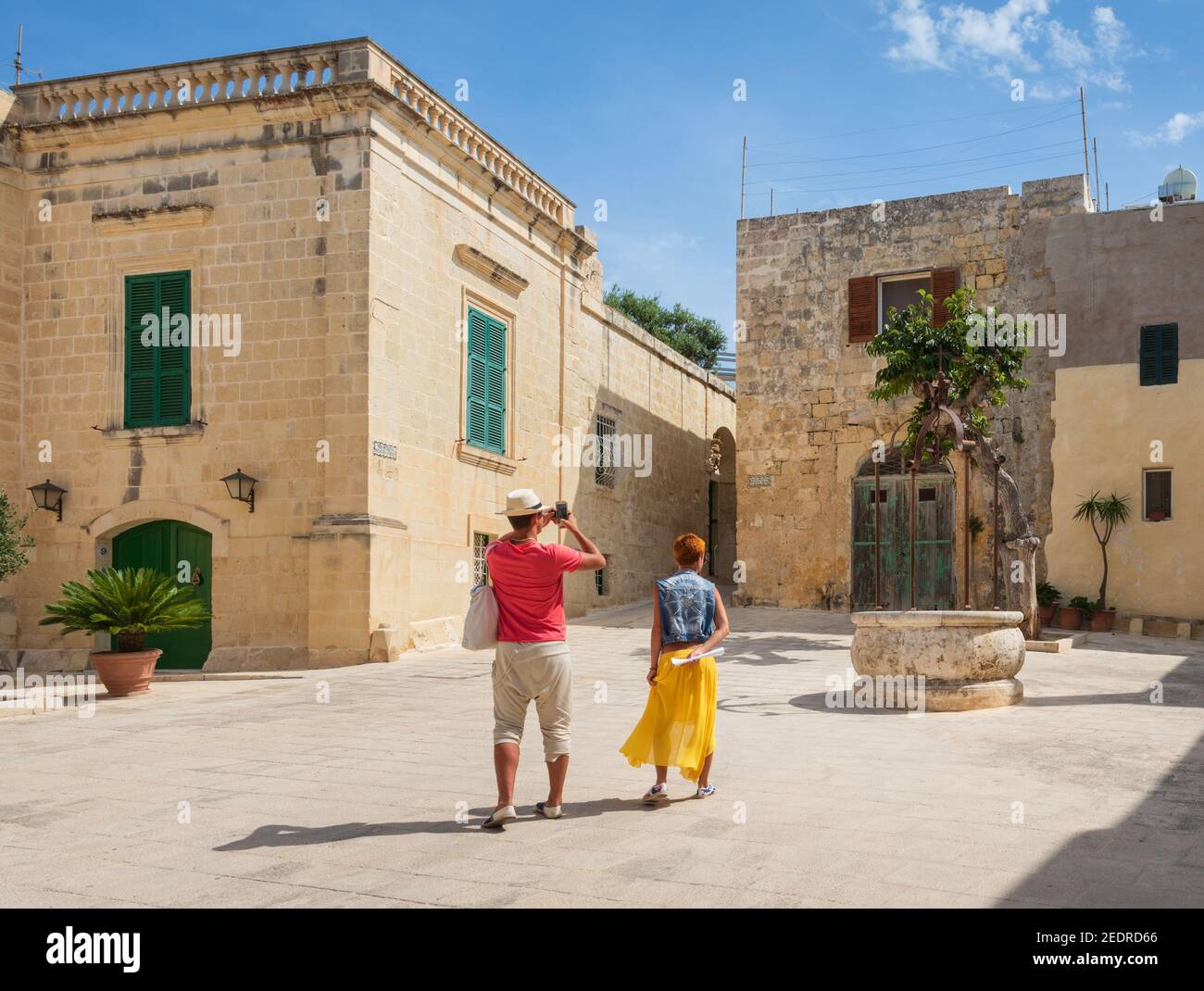 Colourful tourist couple photograph a well in Mesquita Square Mdina Malta Stock Photo